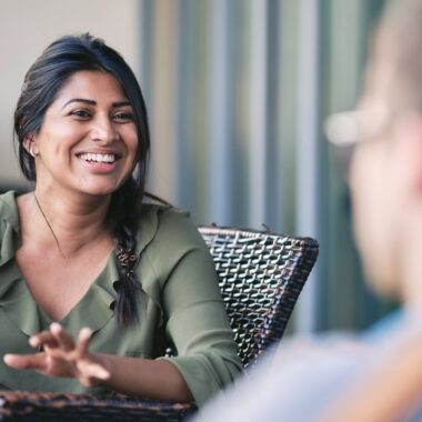 The picture shows a dialog situation with the focus on a smiling women sitting in a chair.