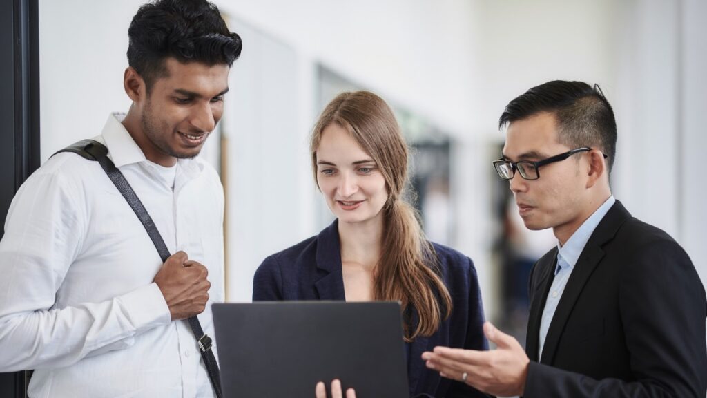 Three HHL students look into a laptop and discuss.