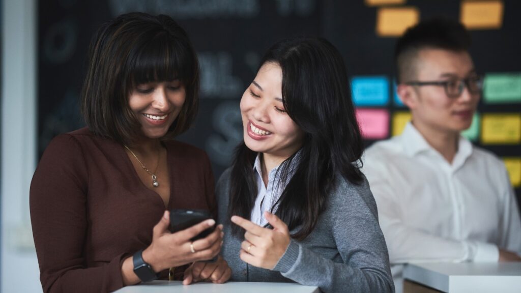 Two female MBA students looking at a smartphone.